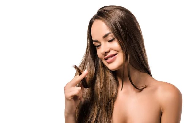 Feliz hermosa mujer sosteniendo largo cabello castaño y mirando consejos aislados en blanco - foto de stock