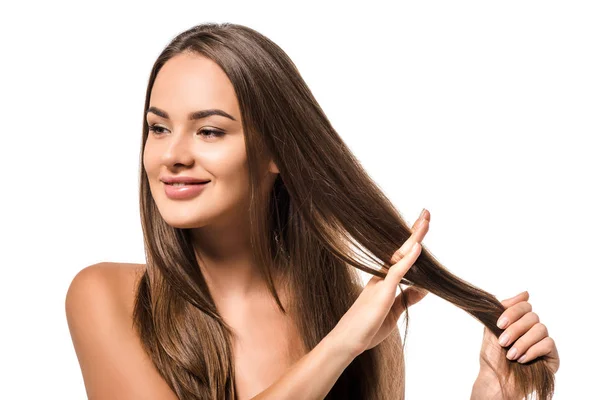 Hermosa mujer sosteniendo largo cabello castaño y sonriendo aislado en blanco - foto de stock