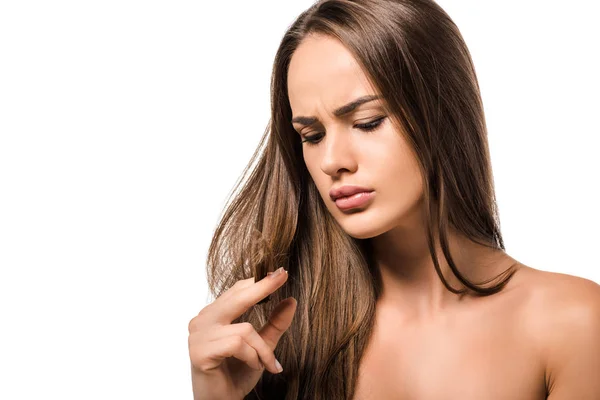 Mujer hermosa preocupada sosteniendo el pelo largo marrón y mirando las puntas aisladas en blanco - foto de stock