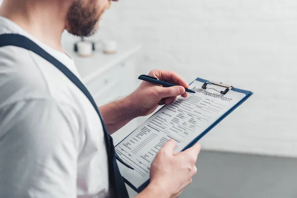 Teilansicht eines erwachsenen Reparateurs, der Notizen im Klemmbrett in der Küche macht — Stockfoto