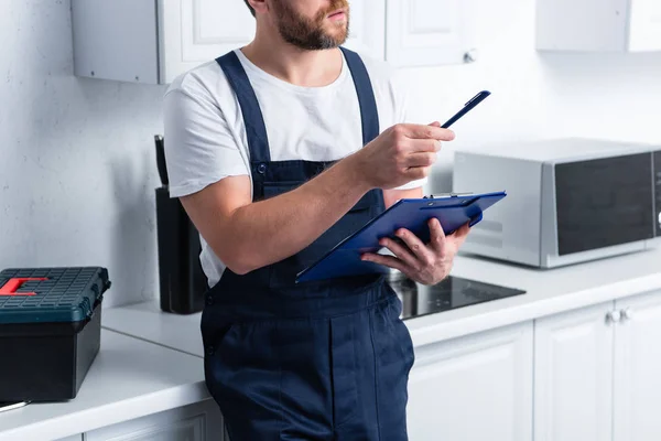 Частковий вид бородатого майстра, який вказує на ручку і тримає буфер обміну на кухні — стокове фото