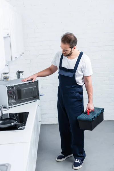 Visão de alto ângulo do faz-tudo adulto com caixa de ferramentas verificando forno de microondas na cozinha — Fotografia de Stock
