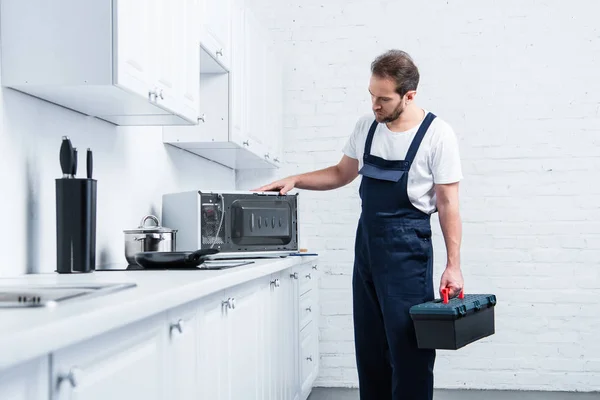 Adulte bricoleur avec boîte à outils vérifier four à micro-ondes dans la cuisine — Photo de stock