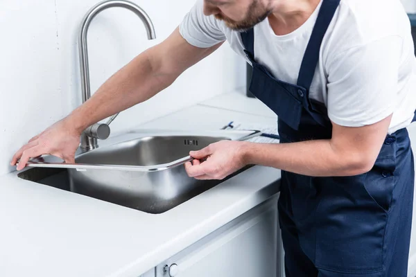 Partial view of bearded repairman in working overall fixing sink in kitchen — Stock Photo