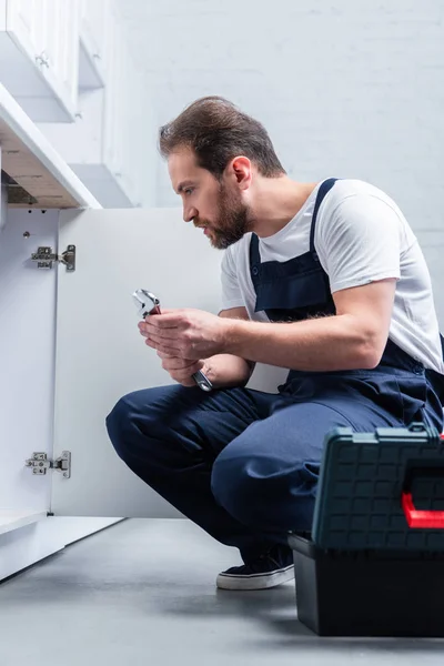 Side view of handyman with pair of nippers checking sink in kitchen — Stock Photo