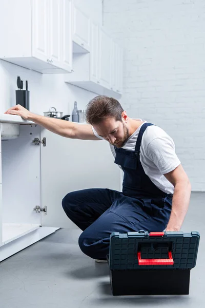 Beau réparateur adulte avec boîte à outils évier de vérification dans la cuisine — Photo de stock