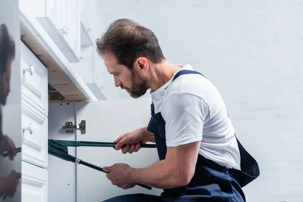 Visão lateral do reparador barbudo adulto em trabalhar pia de fixação geral com par de garras na cozinha — Fotografia de Stock