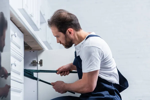 Vista lateral del reparador barbudo adulto en el fregadero de fijación general de trabajo con un par de pinzas en la cocina - foto de stock