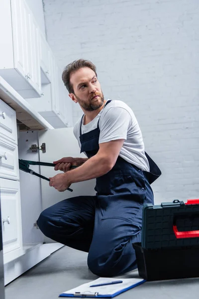 Reparador en el trabajo en general fregadero de fijación con un par de pinzas en la cocina — Stock Photo