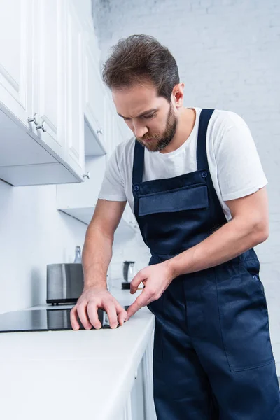 Focused handyman in working overall fixing oven in kitchen — Stock Photo