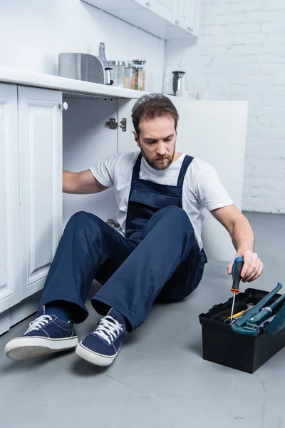 Handyman in working overall fixing oven and taking tools from toolbox in kitchen — Stock Photo