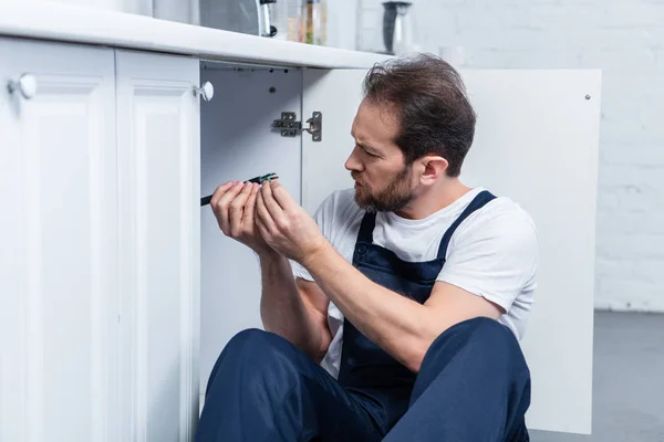 Side view of handyman in working overall fixing wires from oven in kitchen — Stock Photo