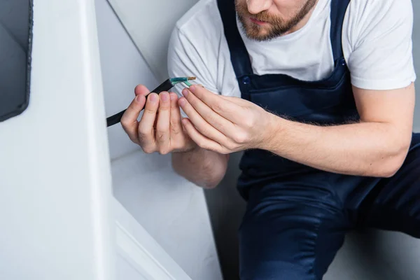 Cropped shot of handyman in working overall fixing wires from oven in kitchen — Stock Photo