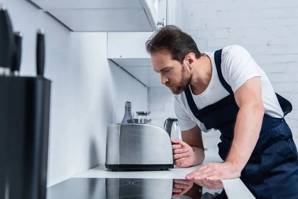 Serious handyman in working overall fixing toaster in kitchen — Stock Photo