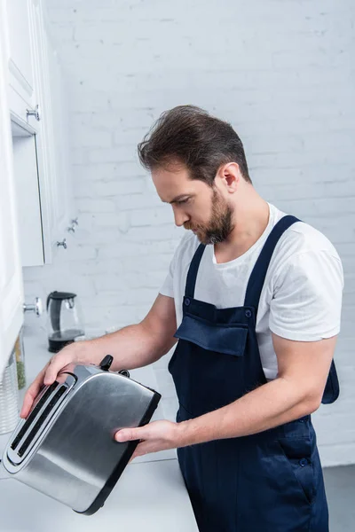 Barbudo artesano en el trabajo en general la fijación de tostadora en la cocina - foto de stock