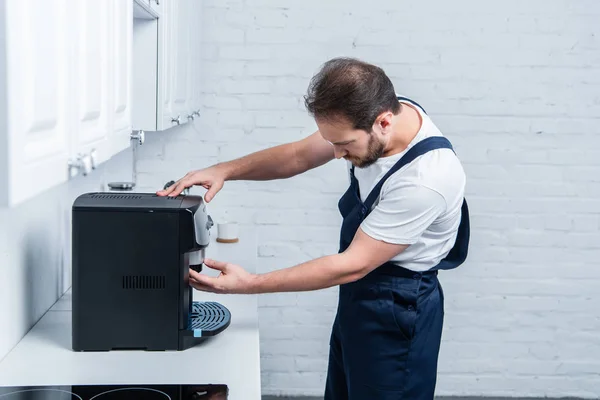 Side view of handyman in working overall repairing coffee machine in kitchen — Stock Photo