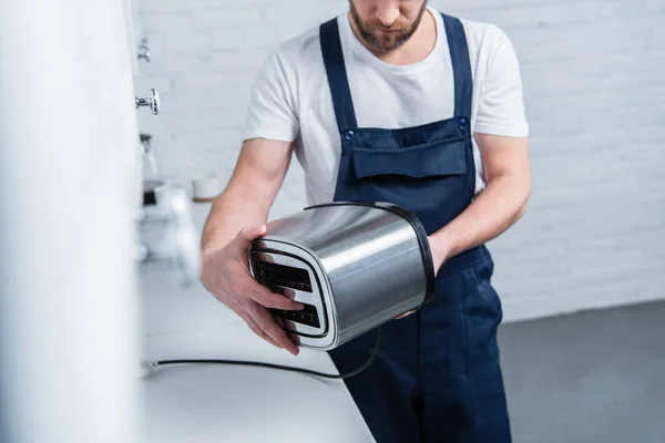 Partial view of bearded craftsman in working overall fixing toaster in kitchen — Stock Photo