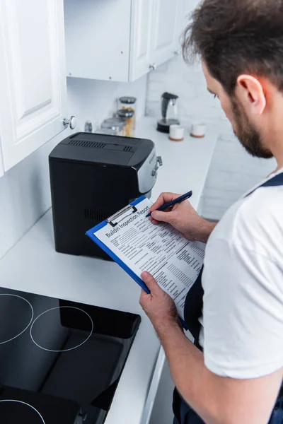 Colpo ritagliato di artigiano che prende appunti negli appunti vicino alla macchina del caffè rotta in cucina — Foto stock