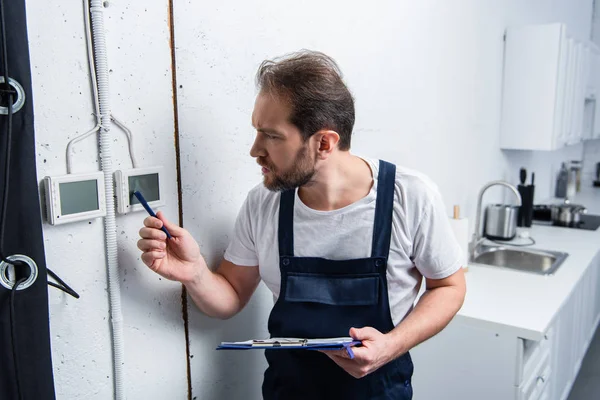 Eletricista adulto concentrado com prancheta verificando painel elétrico — Fotografia de Stock