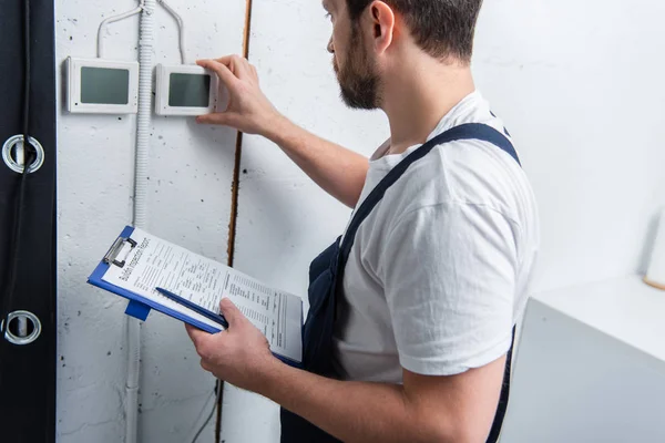 Électricien barbu adulte avec presse-papiers vérifiant le panneau électrique — Photo de stock