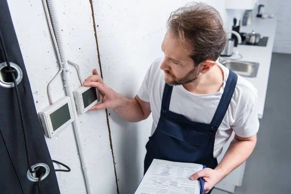 Vista ad alto angolo di elettricista adulto con quadro elettrico di controllo degli appunti — Foto stock