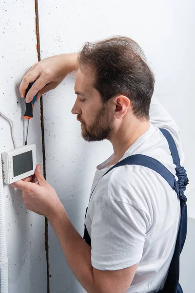 Eletricista masculino com prancheta de fixação caixa elétrica por chave de fenda — Fotografia de Stock