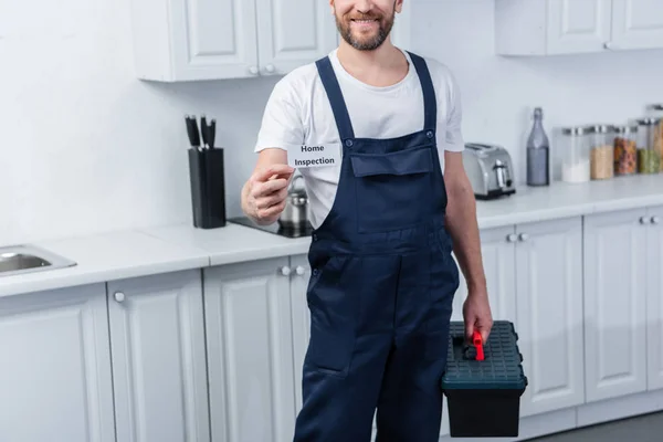 Partial view of male handyman holding toolbox and showing card with lettering home inspection — Stock Photo