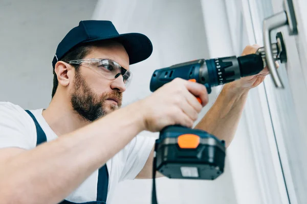 Réparateur adulte en lunettes de fixation poignée de fenêtre par perceuse électrique — Photo de stock