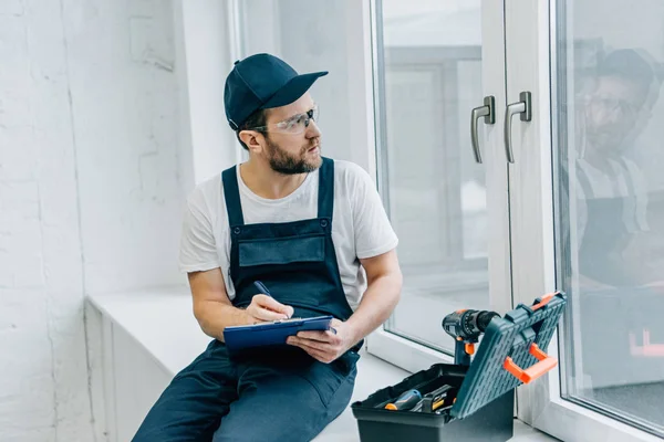 Handwerker mit Brille schreibt in Klemmbrett und überprüft Fenster — Stockfoto