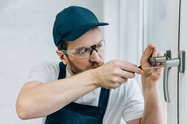 Handwerker in Schutzbrille fixiert Fenstergriff mit Schraubenzieher — Stockfoto