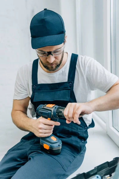 Serious male handyman with electric drill sitting on windowsill — Stock Photo