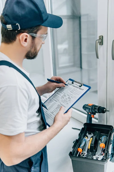 Rückansicht eines erwachsenen Reparateurs, der in Klemmbrett schreibt und Fenster überprüft — Stockfoto