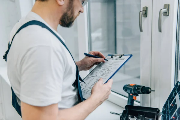 Cropped shot of male handyman writing in clipboard and checking window — Stock Photo