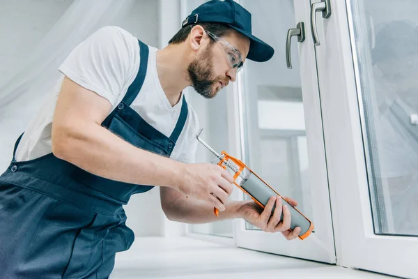 Бородатый ремонтник чинит окно герметичным пистолетом — стоковое фото