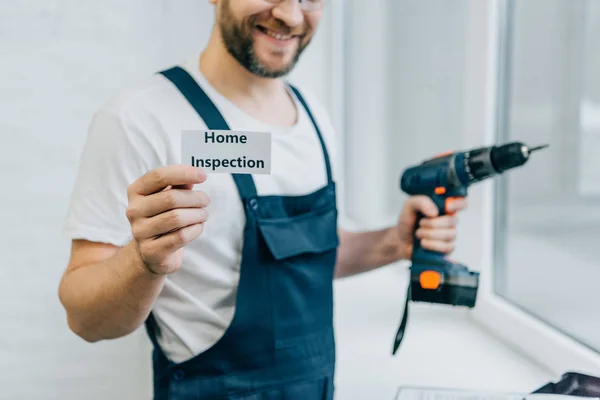 Partial view of male craftsman holding electric drill and showing card with lettering home inspection — Stock Photo