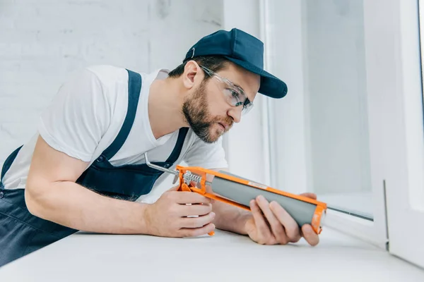 Concentrated adult repairman fixing window with sealant gun — Stock Photo