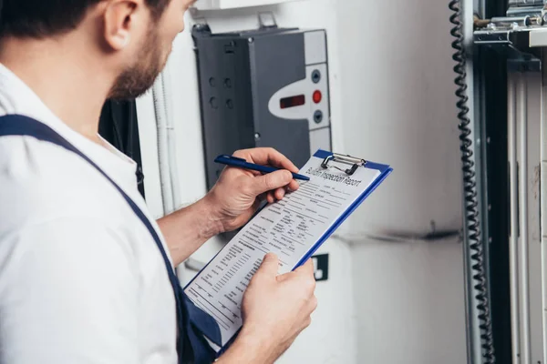 Vista parcial de la escritura masculina del electricista en portapapeles y comprobación de la caja eléctrica - foto de stock