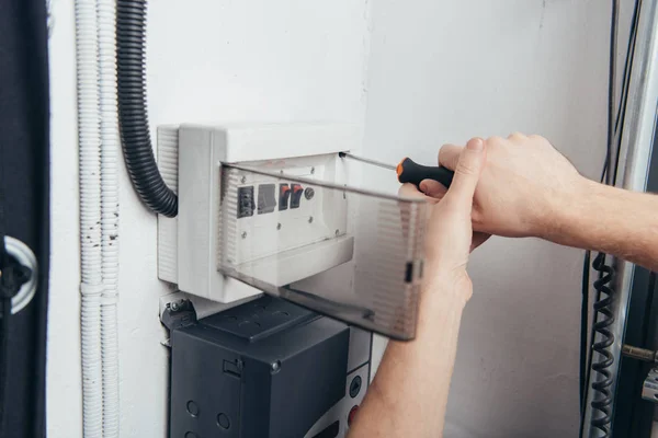 Abgeschnittenes Bild eines männlichen Elektrikers, der einen Stromkasten mit einem Schraubenzieher repariert — Stockfoto