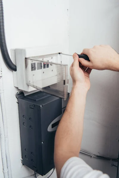 Teilansicht eines männlichen Elektrikers, der einen Stromkasten mit einem Schraubenzieher repariert — Stockfoto