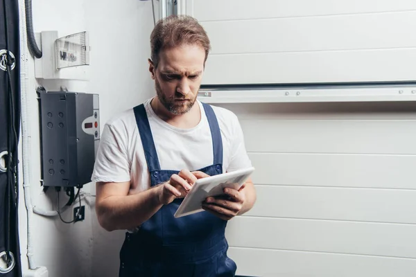 Serio elettricista adulto utilizzando tablet digitale vicino alla scatola elettrica — Foto stock