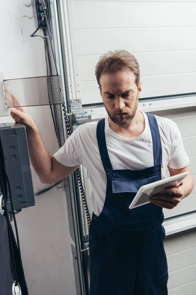 Mann mit Vollbart und digitalem Tablet checkt Stromkasten — Stockfoto