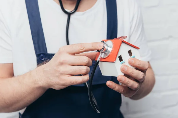 Tiro cortado do artesão verificando figura da casa por estetoscópio, conceito de inspeção em casa — Fotografia de Stock