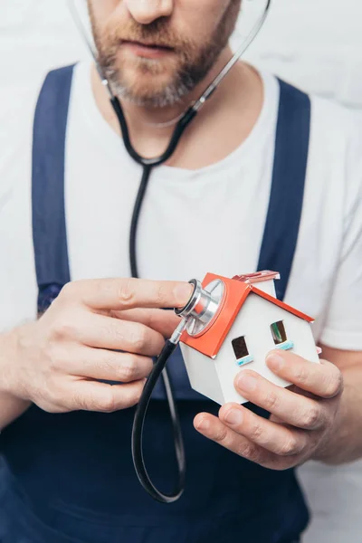 Teilansicht des bärtigen männlichen Reparateurs, der die Hausfigur per Stethoskop überprüft, Inspektionskonzept — Stockfoto