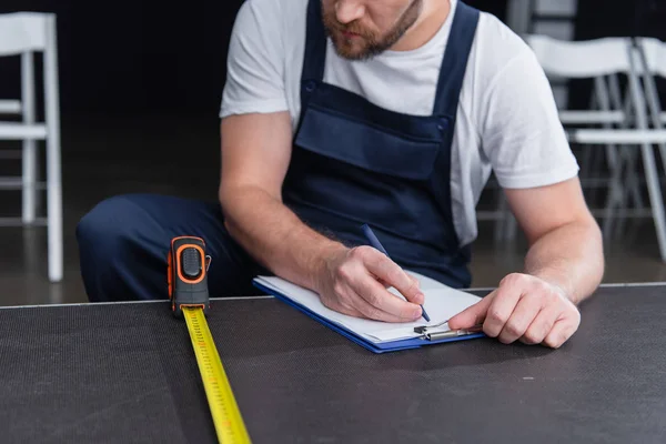 Cropped image of male handyman making measurements and writing in clipboard — Stock Photo