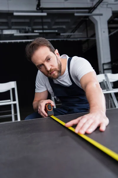 Focused male craftsman in working overall making measurements of floor by measuring tape — Stock Photo