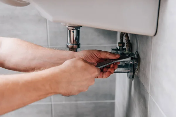 Tiro recortado de plomero masculino en el trabajo en general fregadero de fijación por llave en el baño - foto de stock