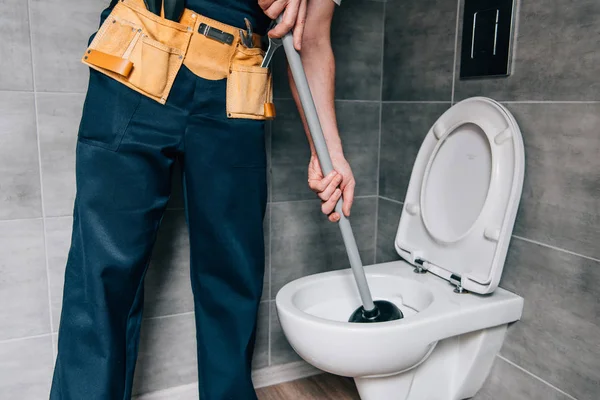 Частичный вид на мужчину сантехника с помощью вантуза и уборка туалета в ванной комнате — стоковое фото
