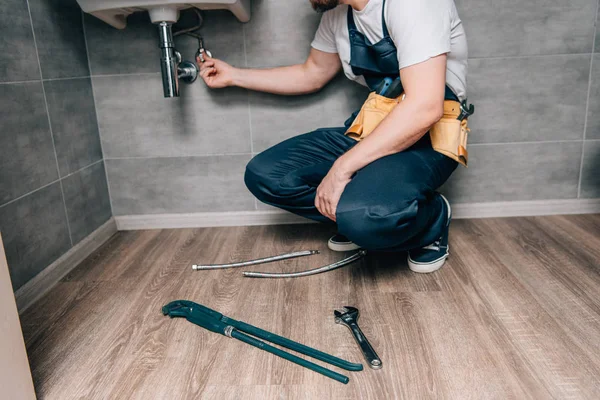 Tiro recortado de plomero masculino con el fregadero de reparación de la correa de herramientas en el baño - foto de stock