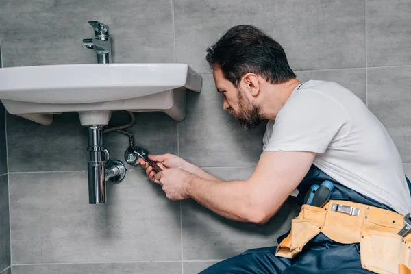 Vista lateral do encanador masculino no trabalho pia de fixação geral por chave na casa de banho — Fotografia de Stock