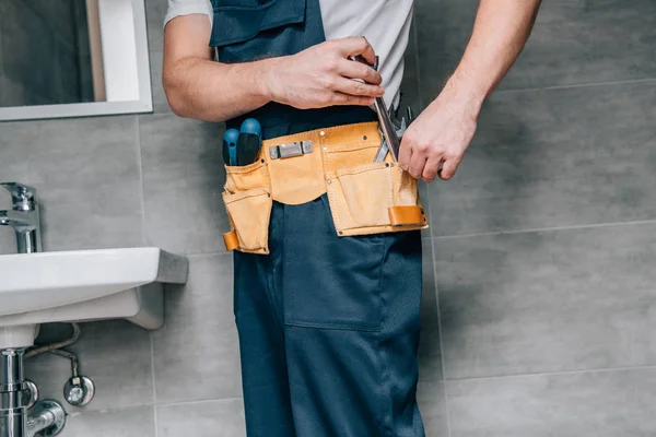 Tiro recortado de plomero masculino poner llave en el cinturón de herramientas en el baño - foto de stock